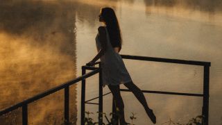 Woman Leaning against Railing By a Pond